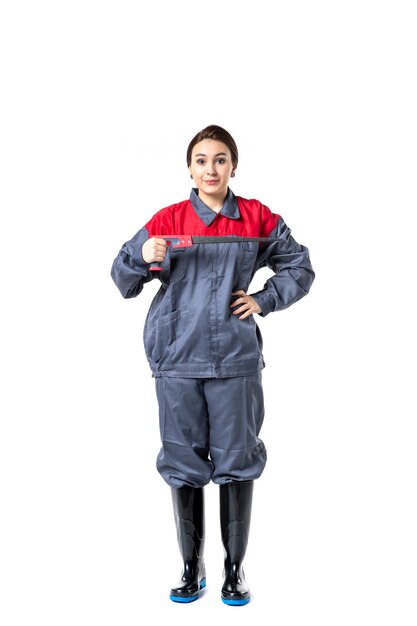 vue de face d'une jeune femme en uniforme spécial tenant une scie à métaux sur un mur blanc