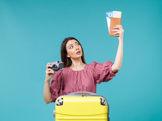 Vue de face jeune femme va en vacances tenant la caméra et des billets sur fond bleu voyage vacances femme à l'étranger mer