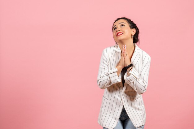 Vue de face jeune femme avec veste blanche priant sur fond rose émotions de la femme mode sentiment femme couleur