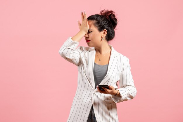 Vue de face jeune femme en veste blanche tenant un téléphone sur fond rose mode femme émotion sentiment couleur dame