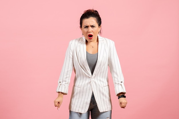 Vue de face jeune femme avec veste blanche et visage en colère sur fond rose émotions femme mode couleur sentiment femme