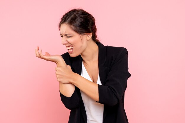 Vue de face jeune femme en veste sombre avec bras blessé sur fond rose