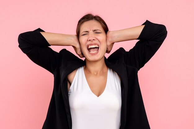 Vue de face jeune femme en veste sombre couvrant ses oreilles sur fond rose