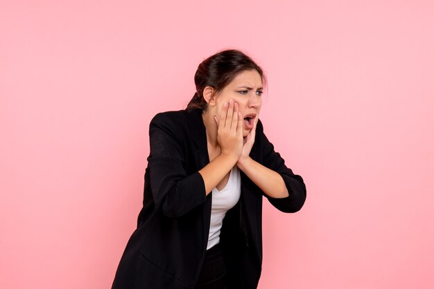 Vue de face jeune femme en veste sombre souffrant de maux de dents sur fond rose