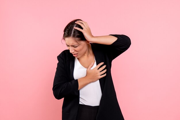 Vue de face jeune femme en veste sombre souffrant de maux de tête sur fond rose