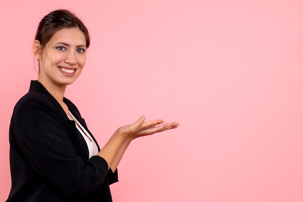 Vue de face jeune femme en veste sombre souriant sur fond rose