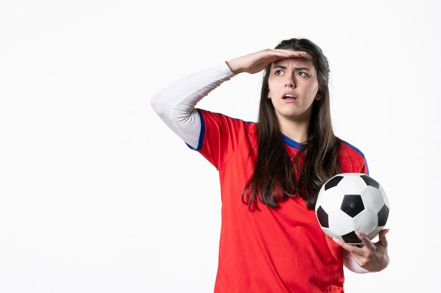 Vue de face jeune femme en vêtements de sport avec ballon de foot sur mur blanc
