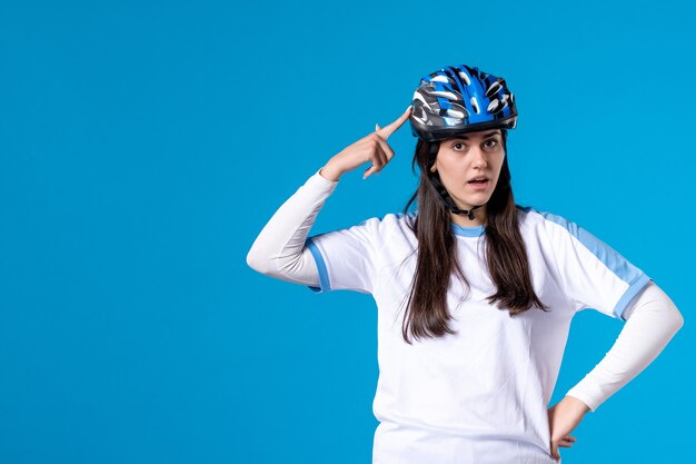 Vue de face jeune femme en vêtements de sport avec casque sur mur bleu