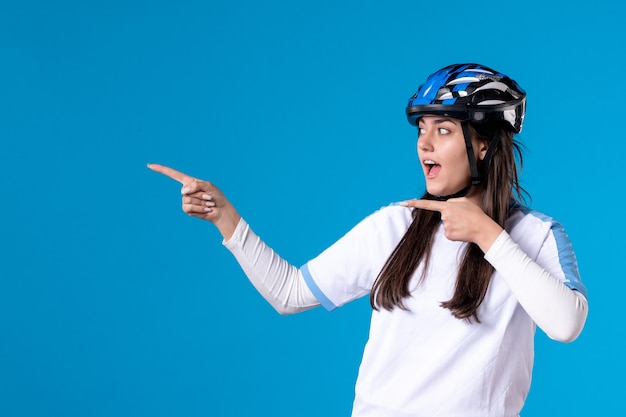 Vue de face jeune femme en vêtements de sport et casque sur mur bleu