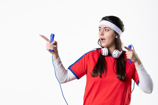 Vue de face jeune femme en vêtements de sport avec des cordes à sauter sur un mur blanc