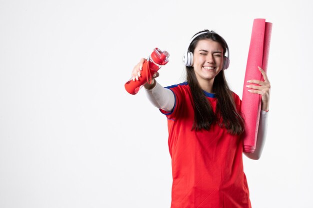 Vue de face jeune femme en vêtements de sport avec des écouteurs mur blanc