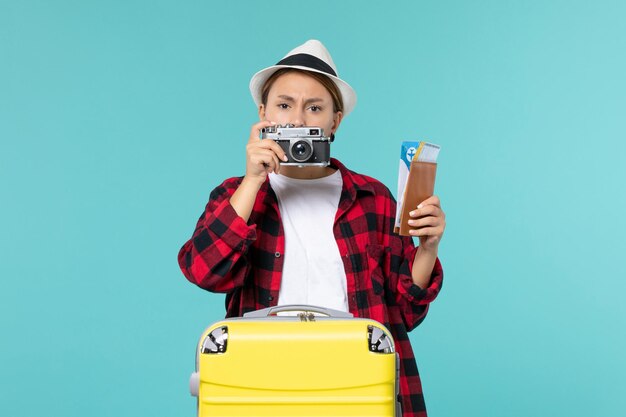 Vue de face jeune femme en voyage tenant des billets et appareil photo sur l'espace bleu