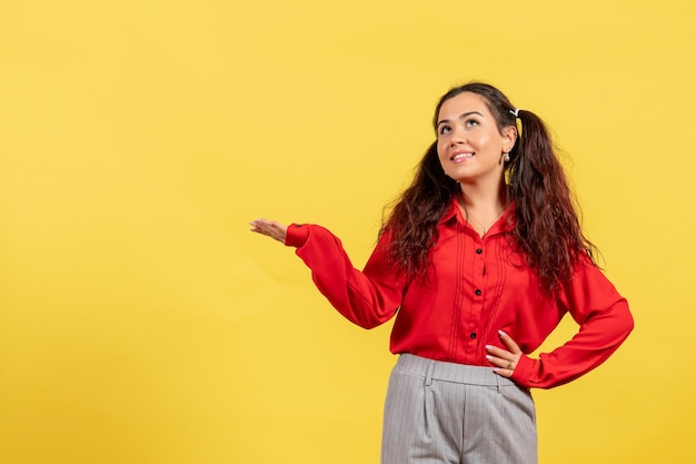 Vue de face jeune fille en blouse rouge avec des cheveux mignons posant sur fond jaune enfant fille jeunesse innocence couleurs kid