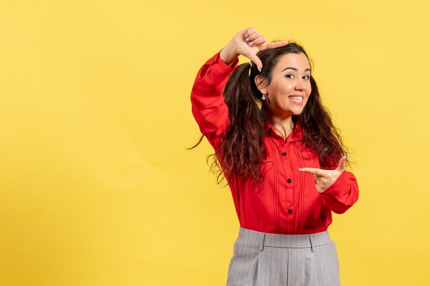 Vue de face jeune fille en blouse rouge avec des cheveux mignons souriant sur fond jaune innocence enfant fille jeunesse couleur enfant