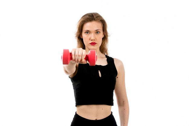 Une vue de face jeune fille en chemise noire et pantalon noir faisant du sport avec des haltères rouges sur le blanc