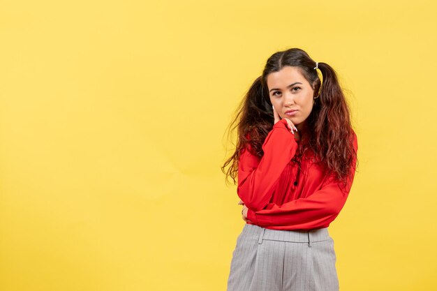 Vue de face jeune fille en chemisier rouge avec des cheveux mignons juste debout sur fond jaune enfant enfant fille jeunesse innocence couleur