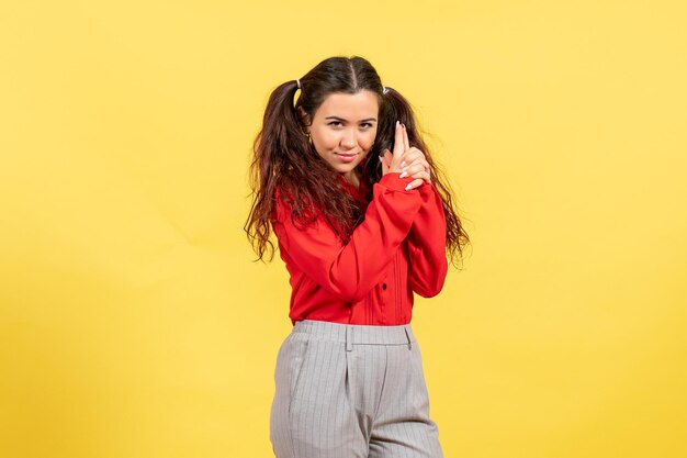 Vue de face jeune fille en chemisier rouge avec pistolet tenant pose sur fond jaune innocence enfant jeunesse enfant fille femme