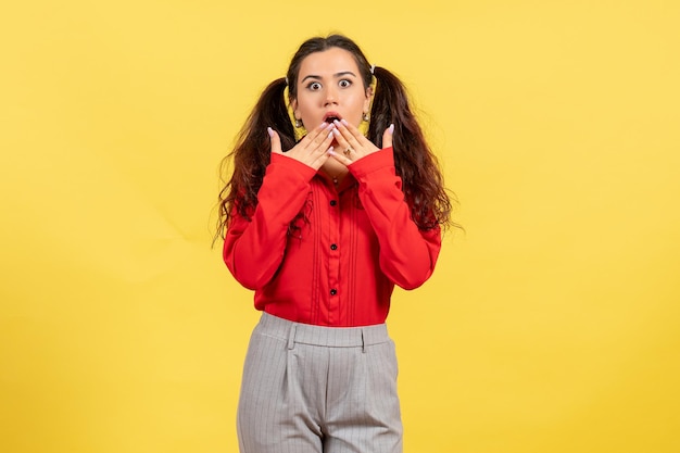 Vue de face jeune fille en chemisier rouge avec visage surpris sur fond jaune couleur innocence enfant jeunesse kid girl