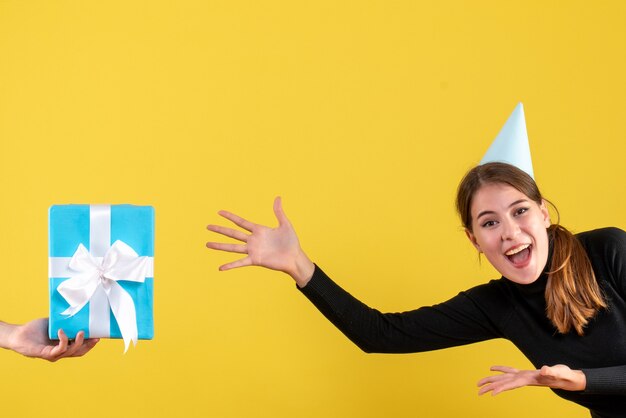 Vue de face jeune fille heureuse avec chapeau de fête essayant d'atteindre le coffret cadeau