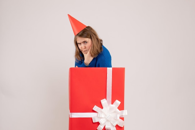 Vue de face d'une jeune fille à l'intérieur d'une boîte cadeau rouge sur un mur blanc