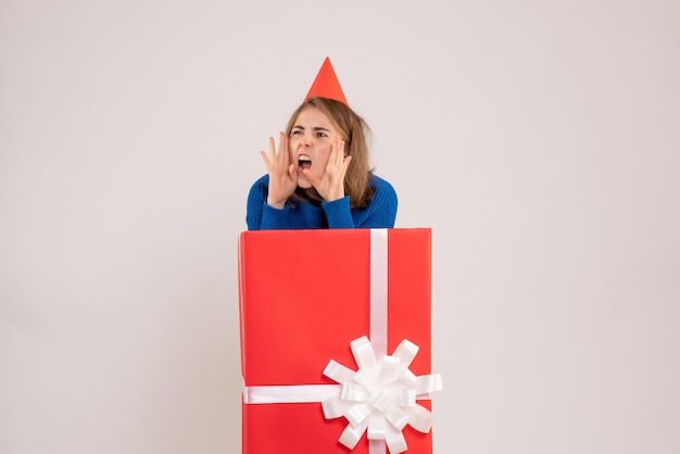 Vue de face d'une jeune fille à l'intérieur d'une boîte cadeau rouge sur un mur blanc