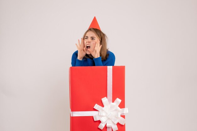 Vue de face d'une jeune fille à l'intérieur d'une boîte cadeau rouge sur un mur blanc