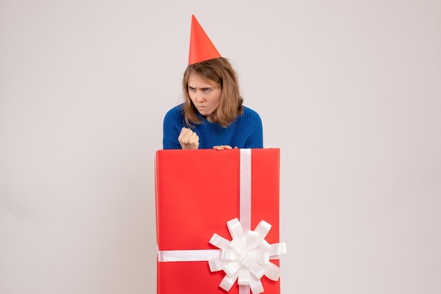 Vue de face d'une jeune fille à l'intérieur d'une boîte cadeau rouge sur un mur blanc