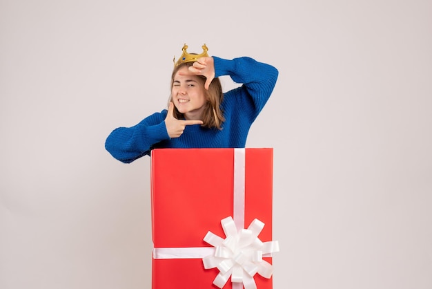 Vue de face d'une jeune fille à l'intérieur d'une boîte cadeau rouge sur un mur blanc