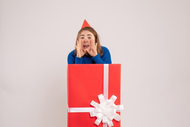 Vue de face d'une jeune fille à l'intérieur d'une boîte cadeau rouge sur un mur blanc