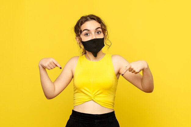 Vue de face de la jeune fille en masque stérile sur mur jaune