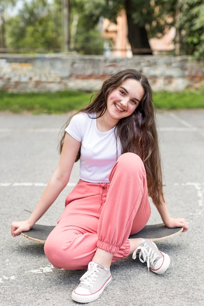 Vue de face jeune fille posant assis sur sa planche à roulettes