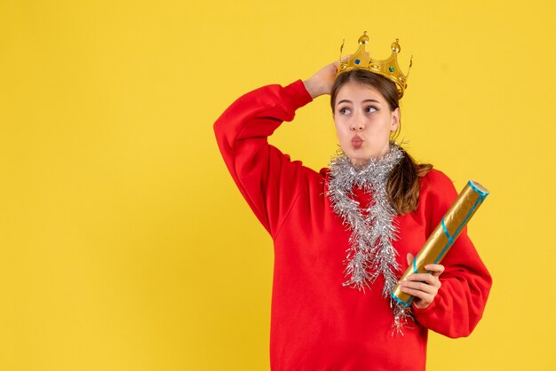 Vue de face jeune fille avec pull rouge tenant popper de fête et sa couronne