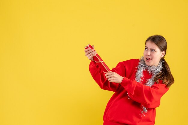 Vue de face jeune fille avec pull rouge tenant popper de fête