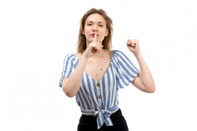 Une vue de face jeune fille séduisante en t-shirt rayé bleu-blanc portant un jean noir posant montrant signe de silence sur le blanc