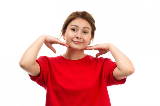 Une vue de face jeune fille séduisante en t-shirt rouge portant un jean noir souriant posant sur le blanc