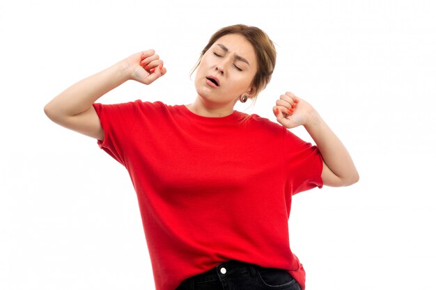 Une vue de face jeune fille séduisante en t-shirt rouge portant des jeans noirs voulant dormir en éternuant sur le blanc