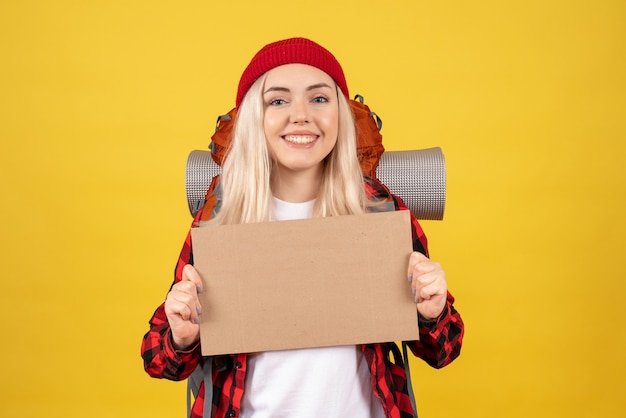 Photo gratuite vue de face jeune fille de voyage avec un chapeau rouge tenant un carton debout sur un mur jaune