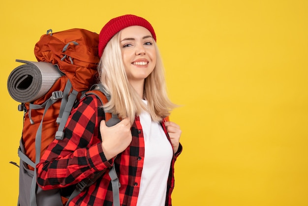 Vue de face jeune fille de voyage avec son sac à dos debout sur un mur jaune