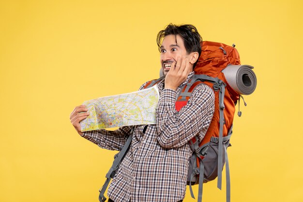 Vue de face jeune homme allant en randonnée avec sac à dos observant la carte sur le voyage aérien de couleur de campus de nature de société de forêt de fond jaune