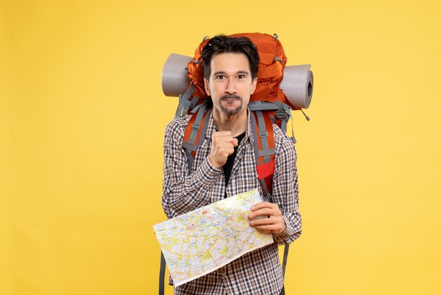 Vue de face jeune homme allant en randonnée avec sac à dos tenant une carte sur fond jaune voyage air nature société campus couleur de la forêt