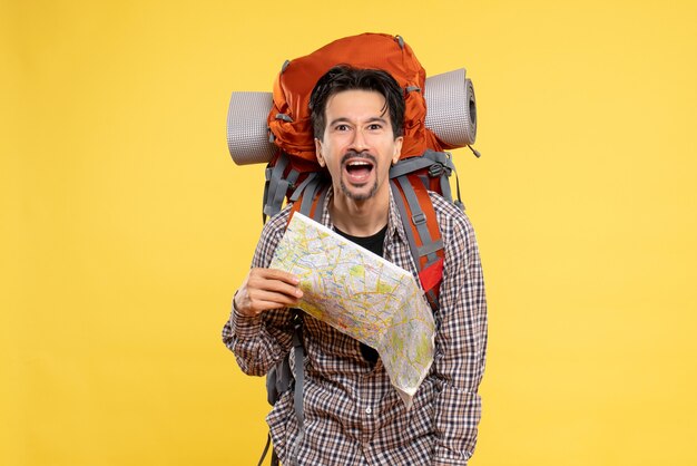 Vue de face jeune homme allant en randonnée avec sac à dos tenant une carte sur fond jaune voyage d'entreprise air nature campus couleur de la forêt