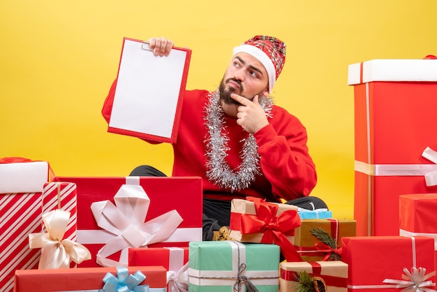 Vue de face jeune homme assis autour de cadeaux sur un bureau jaune