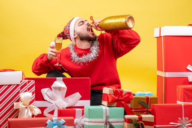 Photo gratuite vue de face jeune homme assis autour de cadeaux avec du champagne sur fond jaune