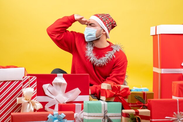 Vue de face jeune homme assis autour de cadeaux sur fond jaune