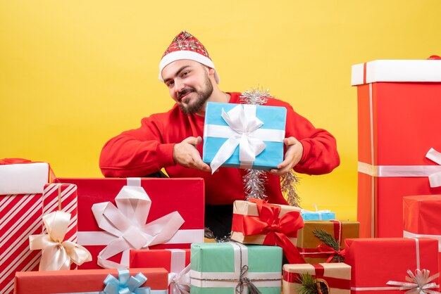 Vue de face jeune homme assis autour de cadeaux sur fond jaune