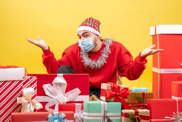 Vue de face jeune homme assis autour de cadeaux sur fond jaune