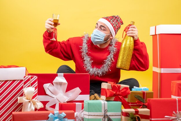 Vue de face jeune homme assis autour de cadeaux sur fond jaune