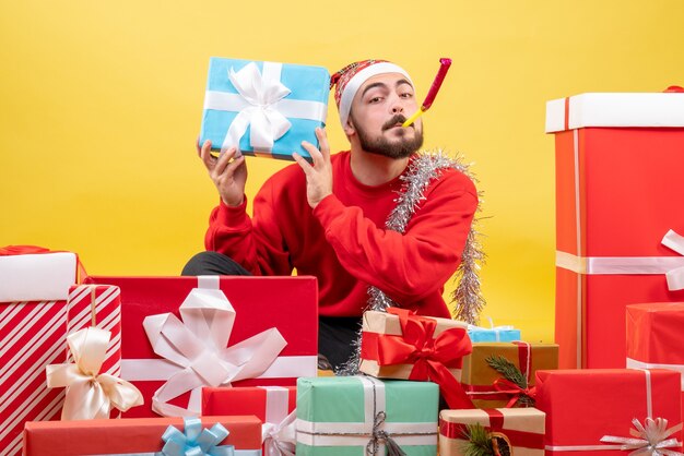 Vue de face jeune homme assis autour de cadeaux sur fond jaune