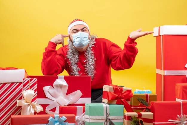 Vue de face jeune homme assis autour de cadeaux en masque sur jaune