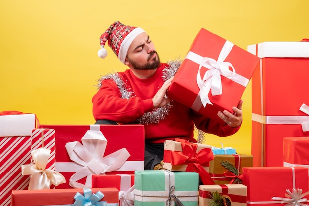 Vue de face jeune homme assis autour de cadeaux de Noël sur fond jaune